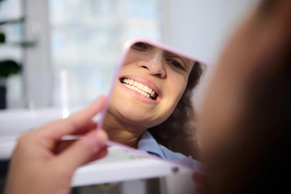 Woman looking at her teeth in a cosmetic mirror